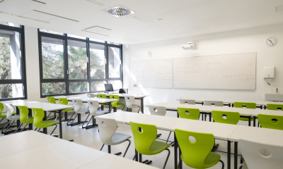 Tuščia klasė, kurioje stovi stalai su kėdėmis, o ant sienos kabo rašymo lenta